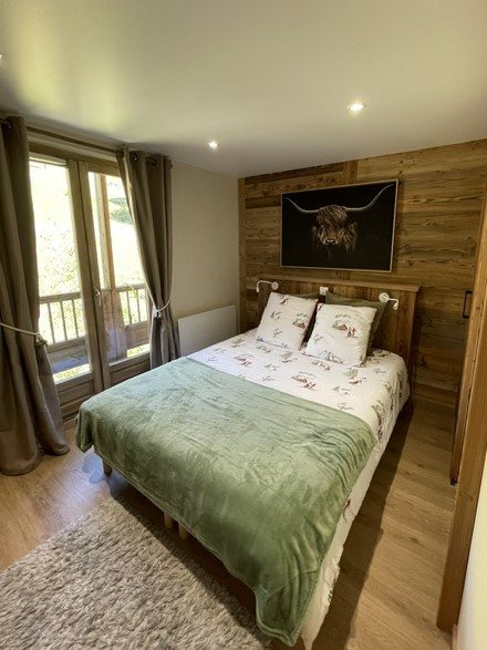 Chambre Bon Amour : lit double, mur en bois avec tableau de vache des Highlands et porte-fenêtre sur le balcon